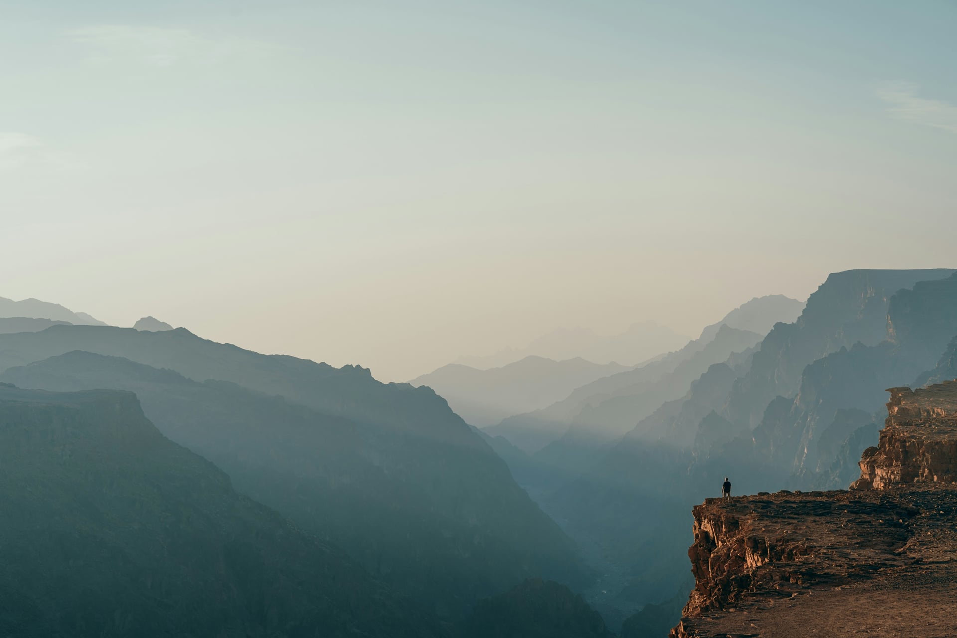 A lone figure standing on a cliff edge above a misty mountain canyon at dawn