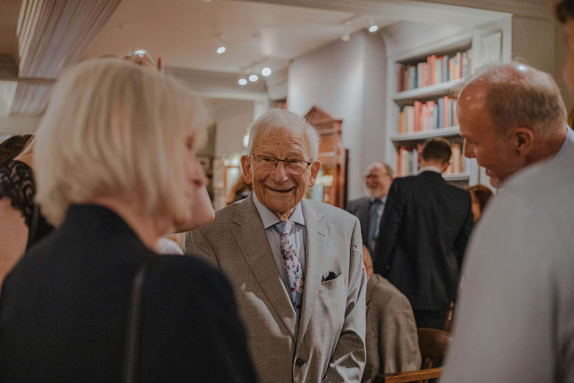 A smiling senior man in a grey suit talking with friends at a gathering
